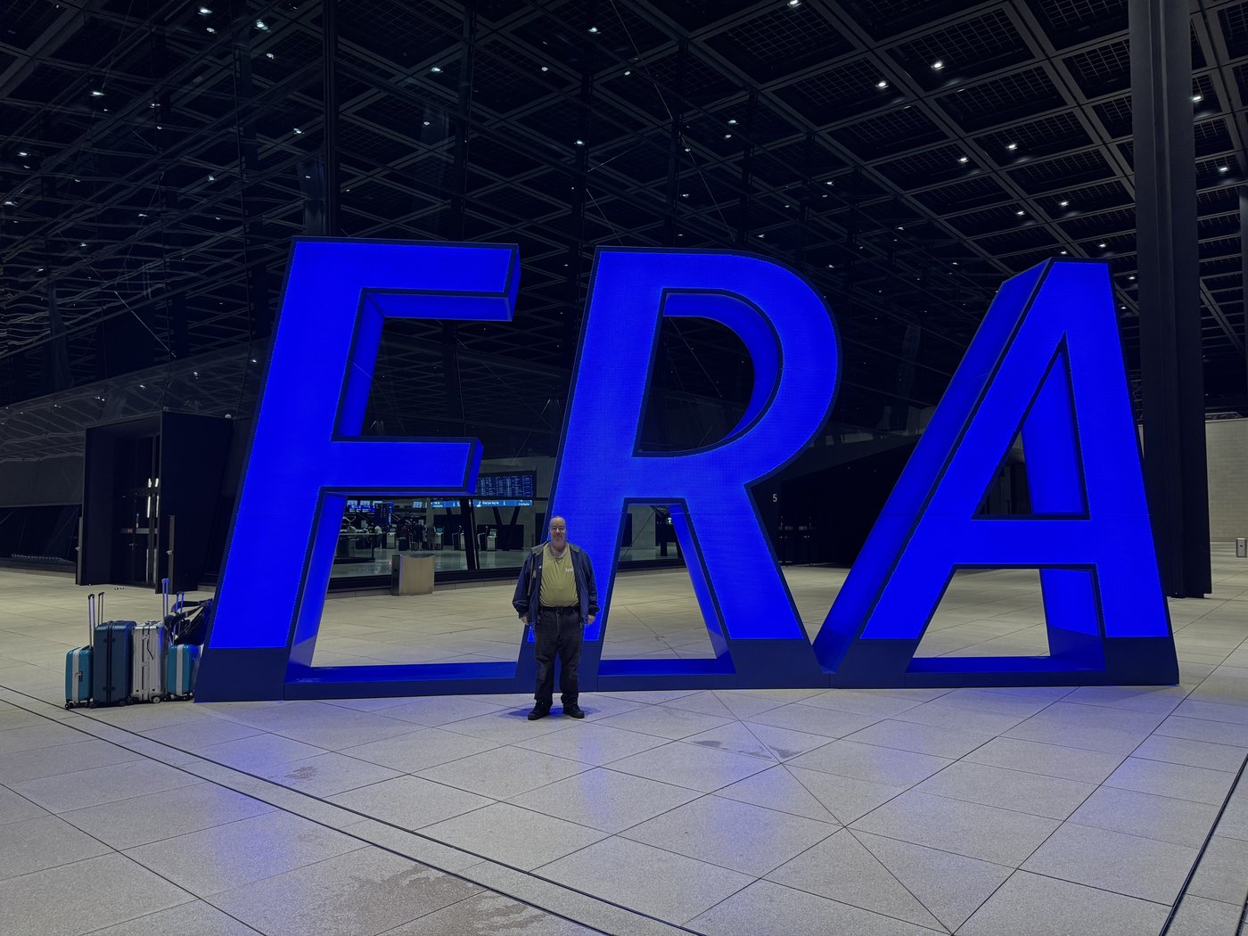 Der große blaue Schriftzug FRA in einer leeren Flughafenhalle bei Nacht, davor eine einzelne Person.