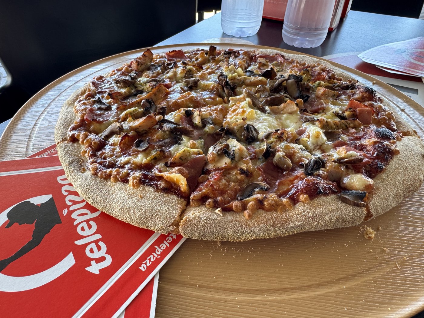 Eine Pizza mit Champignons, Paprika und Fleisch auf einem Teller, daneben eine rote Telepizza-Serviette.