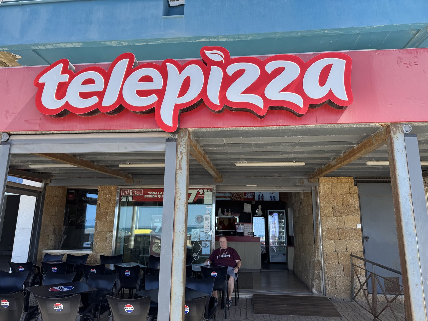Der Eingang eines Telepizza-Lokals mit großem rotem Schriftzug über der offenen Tür, dahinter Tische und Gäste.