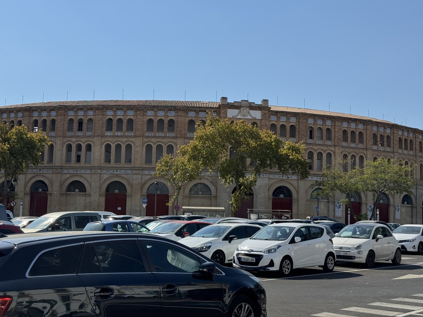 Die Stierkampfarena von El Puerto de Santa María: ein ockerfarbener Rundbau mit umlaufenden Arkaden, davor eine Reihe parkender Autos.