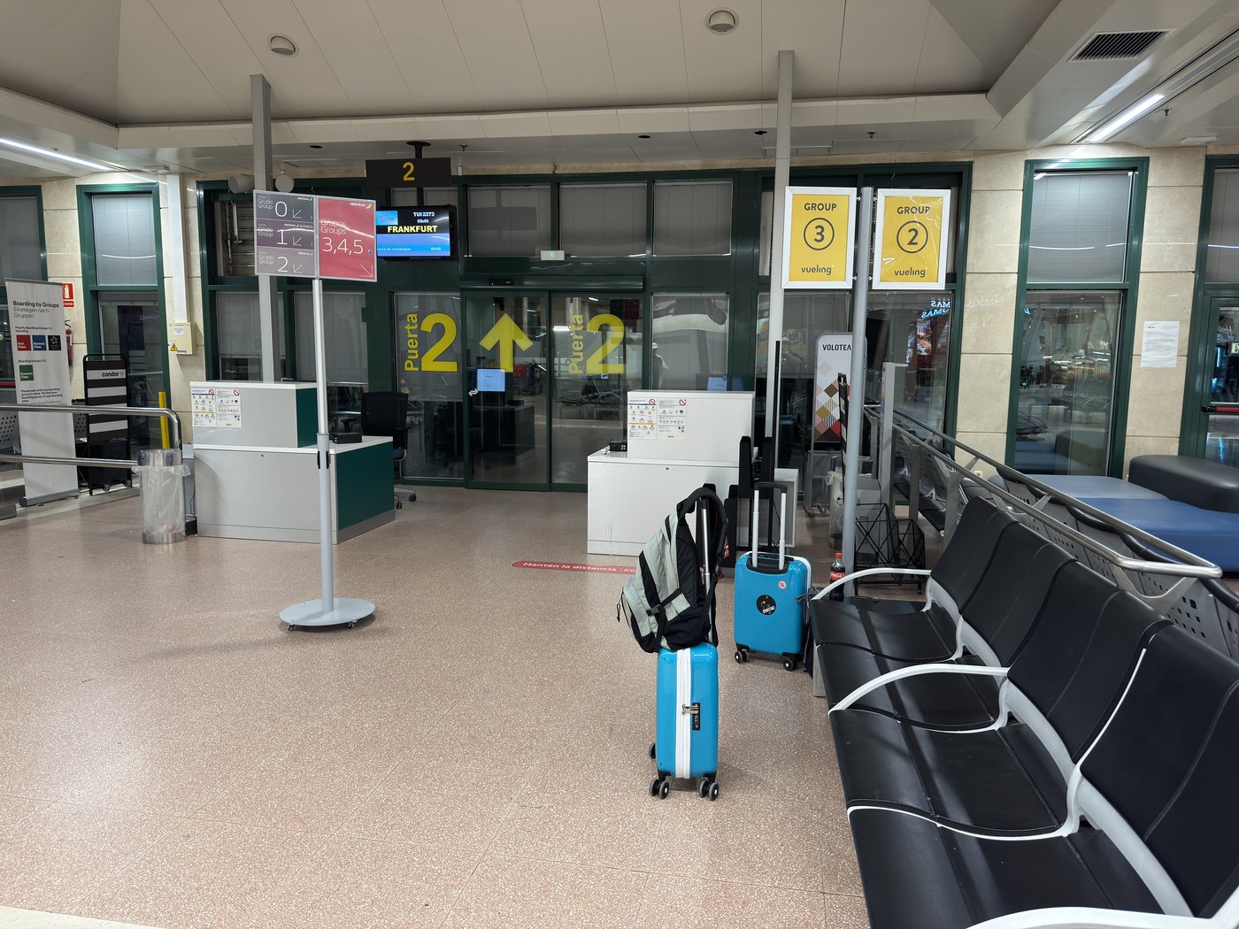 Eine völlig leere Abflughalle mit unbesetzten Check-in-Schaltern, davor zwei abgestellte Koffer und leere Wartebänke.