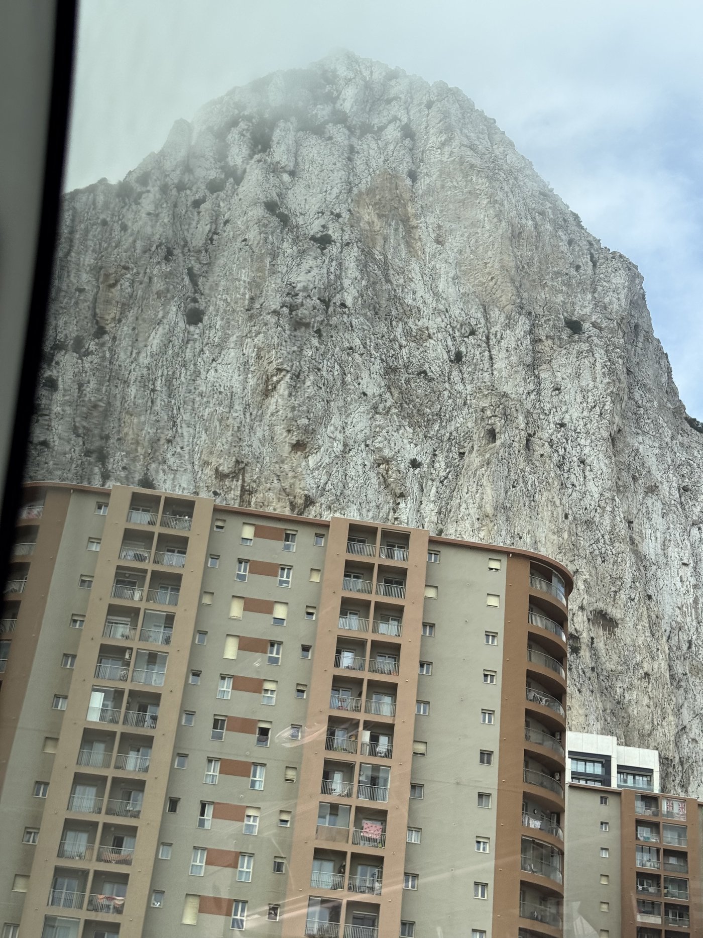 Der Felsen von Gibraltar erhebt sich senkrecht hinter einem Wohnhochhaus; die Steilwand füllt den ganzen Himmel.