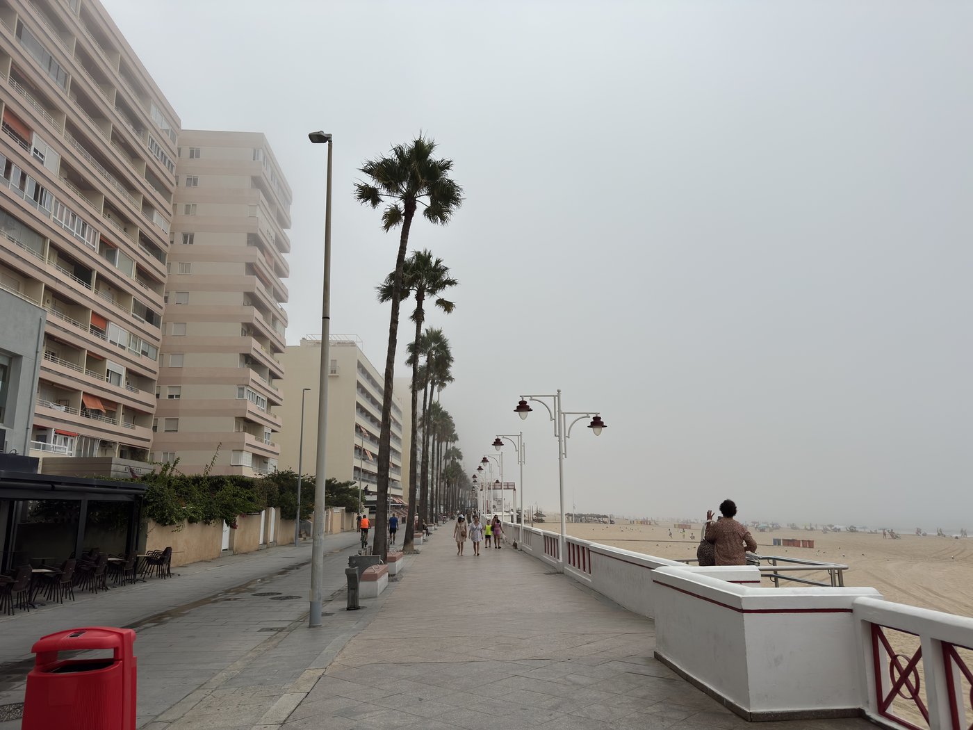 Eine Strandpromenade mit Palmen und Bänken, in dichtem grauem Nebel; Gebäude und Horizont lösen sich nach wenigen Metern auf.