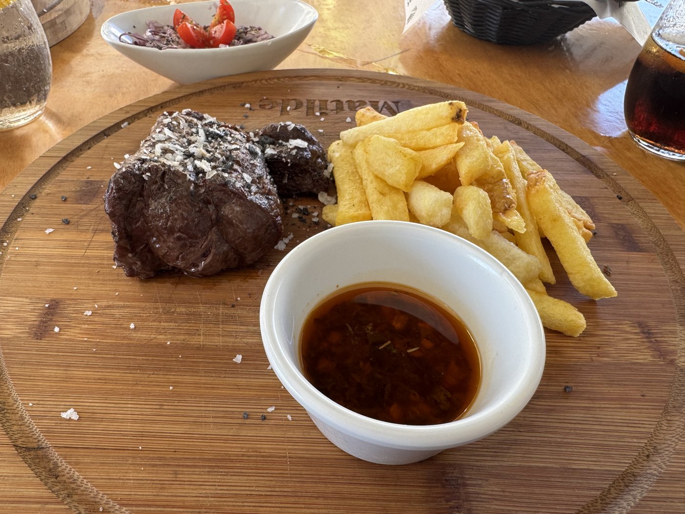 Zwei gebratene Steakmedaillons mit Pommes frites und einem Schälchen dunkler Sauce auf einem hölzernen Servierbrett.