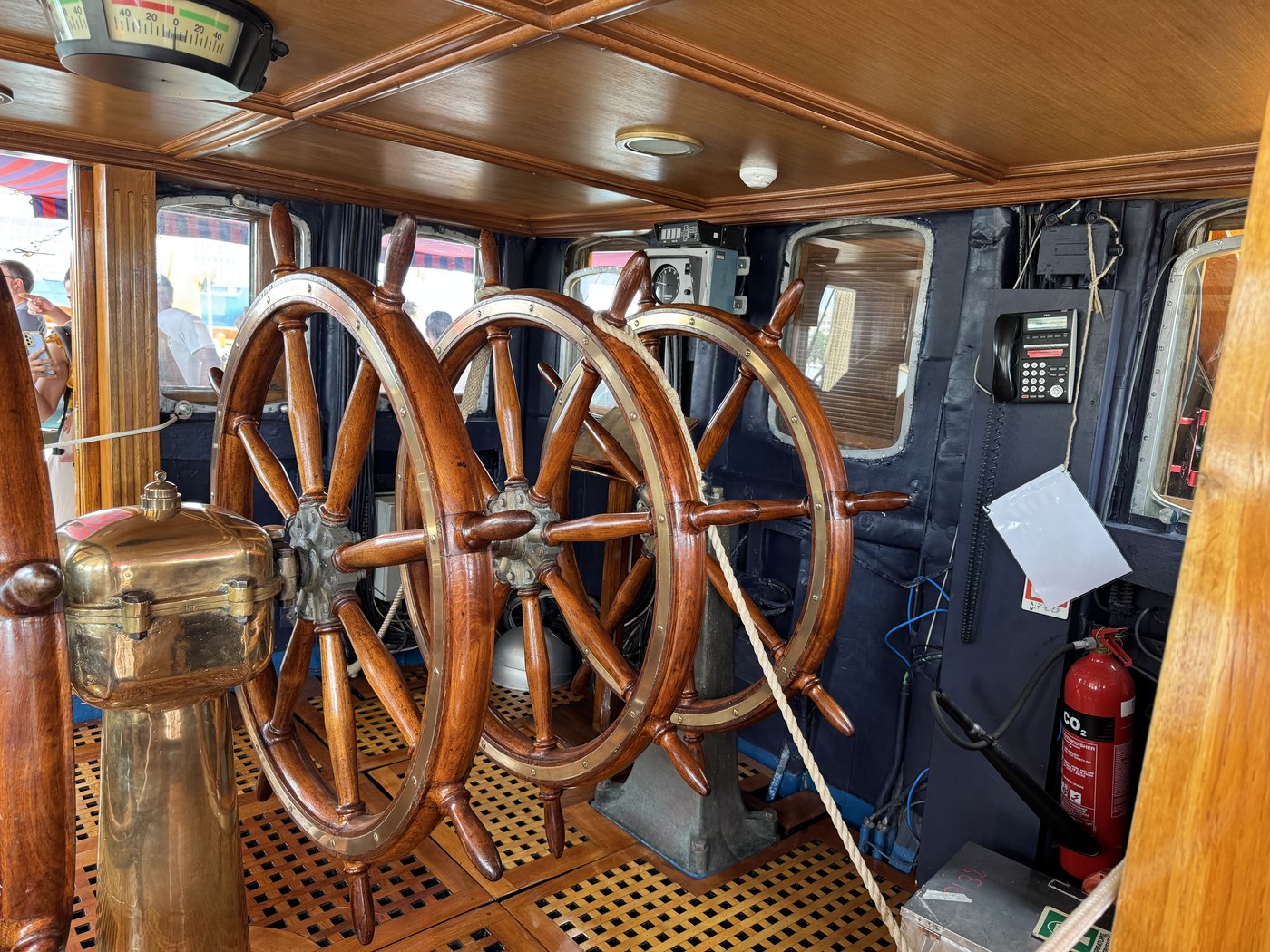 Zwei große hölzerne Doppelsteuerräder hintereinander auf dem Deck eines Segelschulschiffs, dahinter Aufbauten aus lackiertem Holz.