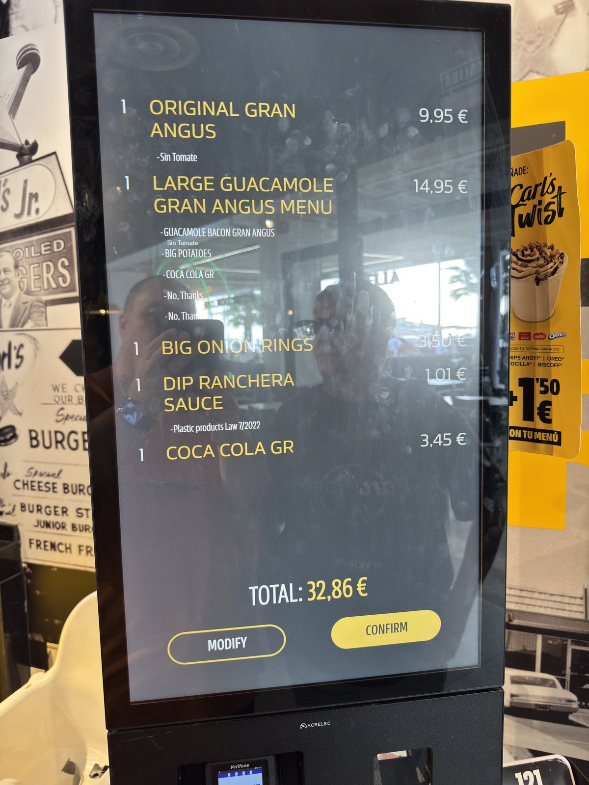 Ein Bestellterminal in einem Schnellrestaurant zeigt eine Menüliste mit Burgern und Preisen, unten eine Schaltfläche mit der Gesamtsumme.