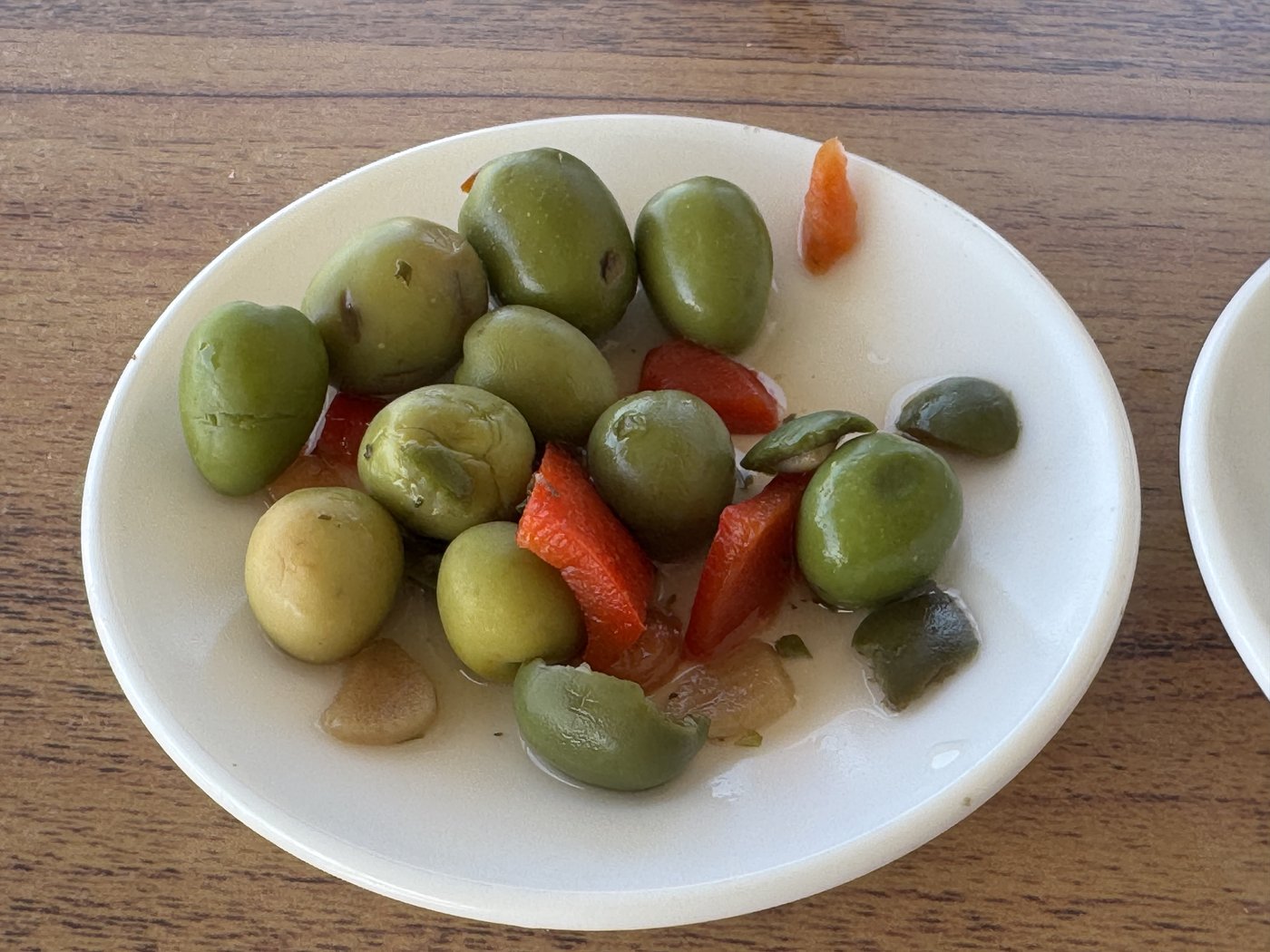Eine weiße Schale mit großen grünen Oliven, dazwischen Stücke von eingelegter Paprika und Karotte.
