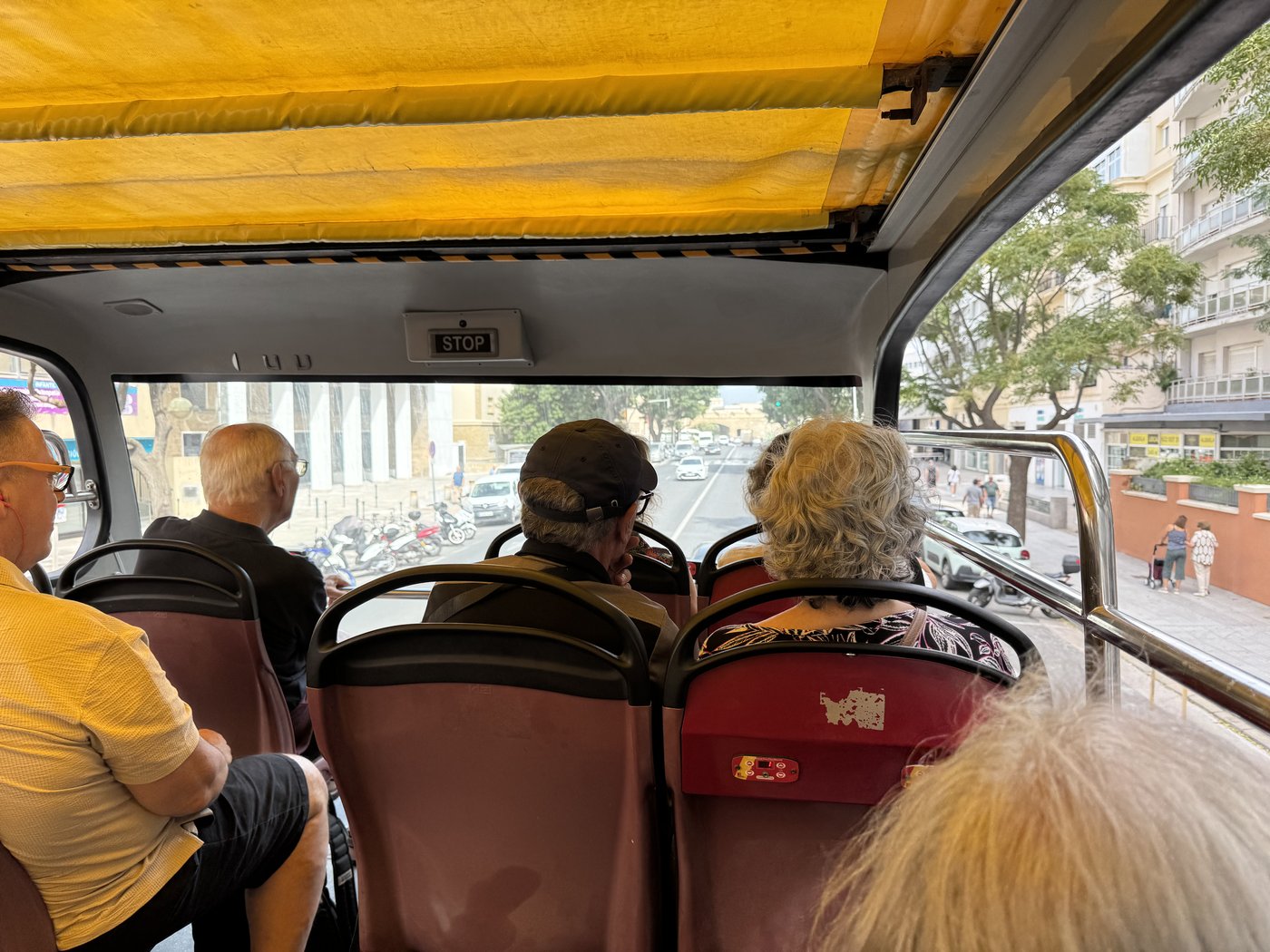 Blick über das Oberdeck eines offenen Stadtrundfahrtbusses mit gelbem Sonnendach und mehreren Fahrgästen.