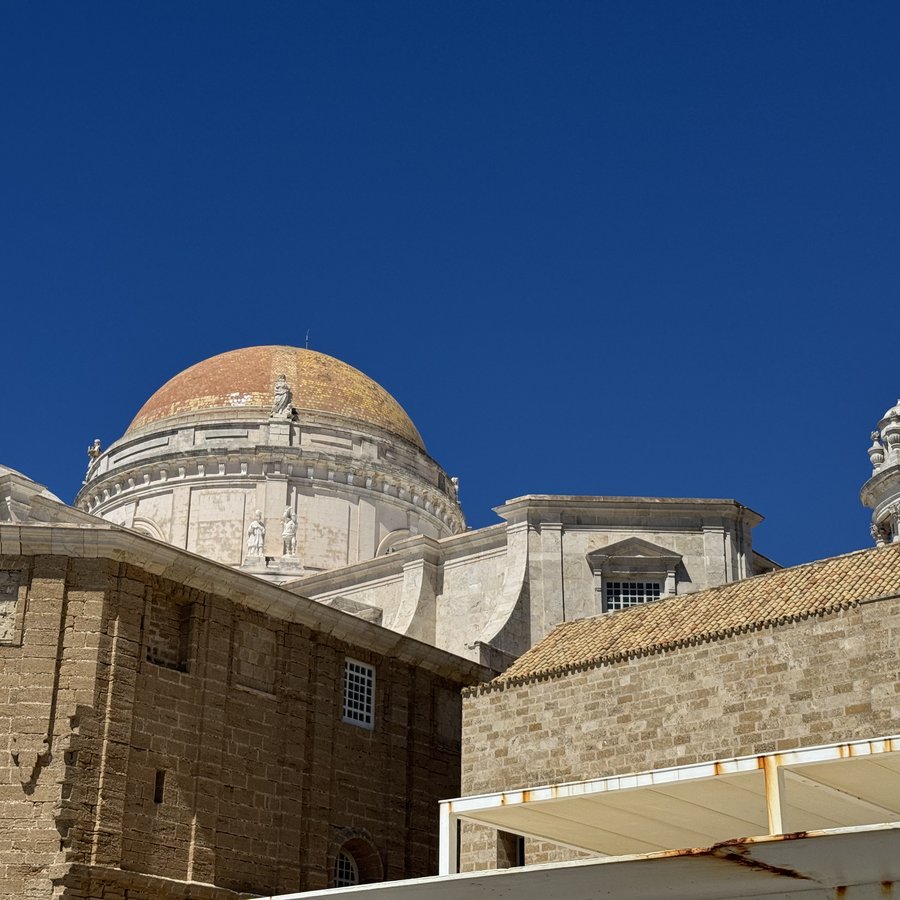 Die Rückseite der Kathedrale von Cádiz: die gelb-goldene Kuppel über hellen Sandsteinmauern vor einem tiefblauen, wolkenlosen Himmel.