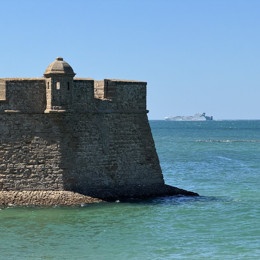 Das Castillo de San Sebastián: eine wuchtige Festungsmauer aus hellem Stein, umspült von türkisfarbenem Wasser.