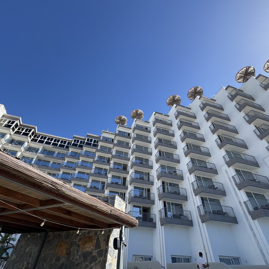 Die Hotelfassade von unten gesehen, weiße Balkonreihen vor tiefblauem Himmel, im Vordergrund ein Sonnenschirm.