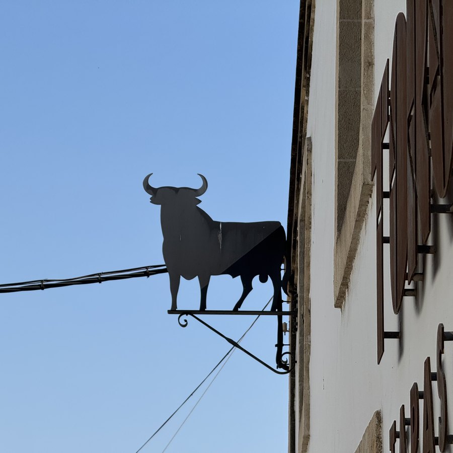 Ein schmiedeeiserner schwarzer Stier als Wandschild an einer weißen Hauswand.
