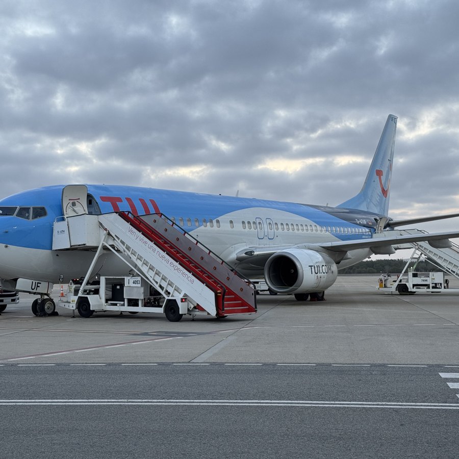 Ein Flugzeug am Flughafen mit ausgefahrener Gangway unter bewölktem Himmel.